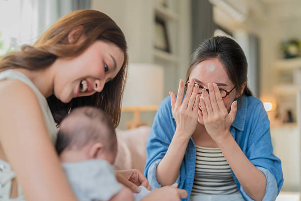 Two women smiling at a baby in a cozy room. One woman playfully covers her face, while the other leans in, creating a joyful mood.