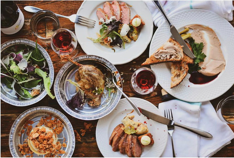 Assorted gourmet dishes with salads and meats on a wooden table, accompanied by red wine. Plates, forks, and napkins are neatly arranged.