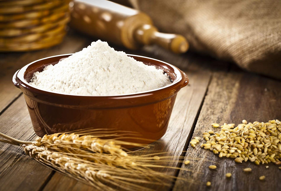 Bowl of flour on a rustic wooden table with wheat stalks, grains, and a rolling pin in the background.