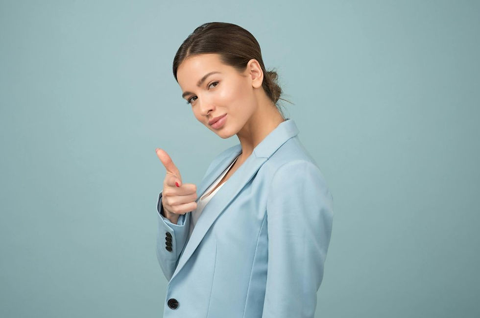 Woman in a light blue suit with a confident smile points finger playfully against a matching blue background.