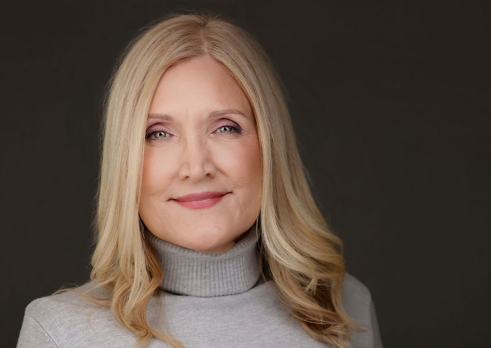 Smiling woman with long blonde hair in a gray turtleneck, set against a dark background, exuding a calm and confident mood.