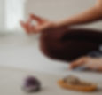 Person meditating with crossed legs, hand in mudra. Sage smokes from a dish, and an amethyst crystal sits nearby on a light surface. Calm mood.
