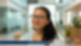 Young woman with glasses smiling in a modern office; potted plants and glass walls in the background. Name tag reads "Parthnia Shenoda."
