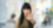 A woman with a serious expression is holding her hand up in a "stop" gesture, with colorful sticky notes blurred in the background.