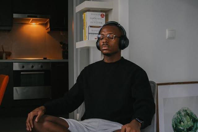 A young man wearing glasses and headphones sits, meditating, with his eyes closed.