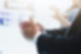 a person in a suit clapping, with blurred individuals in the background also clapping