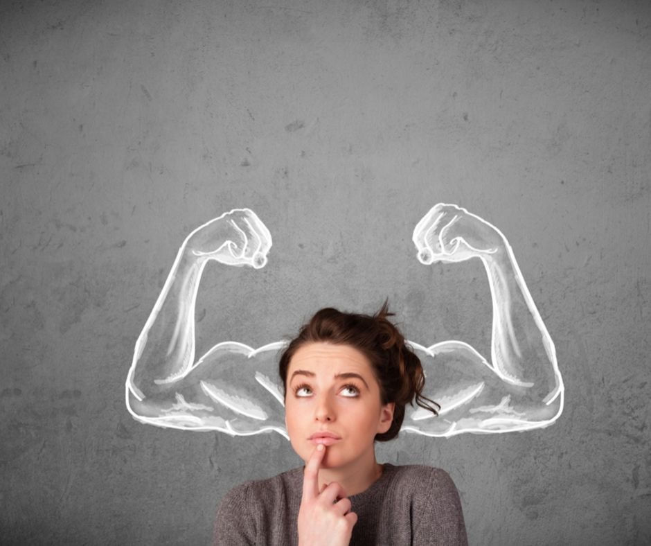 Woman in thought poses, finger on chin, with chalk-drawn muscular arms on a gray background, suggesting inner strength and contemplation.