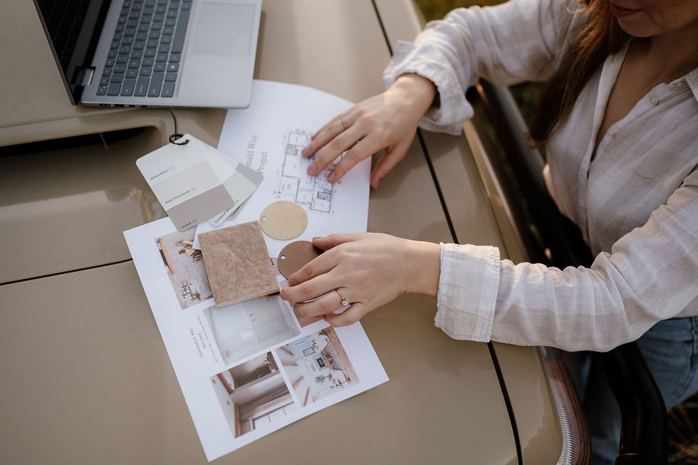 A woman is reviewing interior design plans and material samples on a car bonnet beside an open laptop.