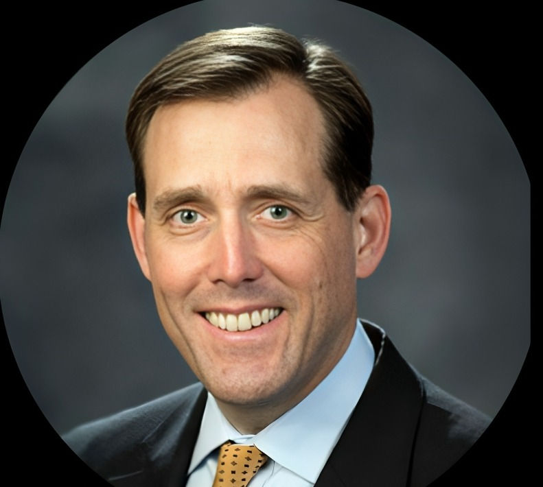Smiling man in a suit and tie against a dark, blurred background, conveying a professional and positive mood.