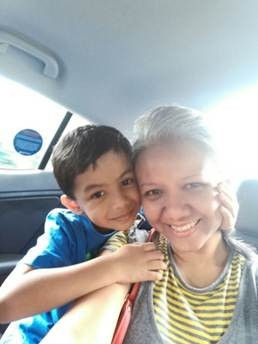 Smiling woman and child in a car, child's arm draped affectionately over her shoulder. Sunlight streams in, creating a warm, joyful mood.