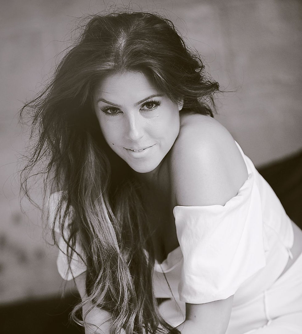 Black-and-white portrait of a woman with long dark hair in an off-shoulder white top, gazing at the camera with a soft smile.