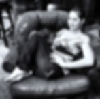 Woman lounging on a leather chair, smiling confidently. Black and white setting with a cozy atmosphere, tiled floor in the background.