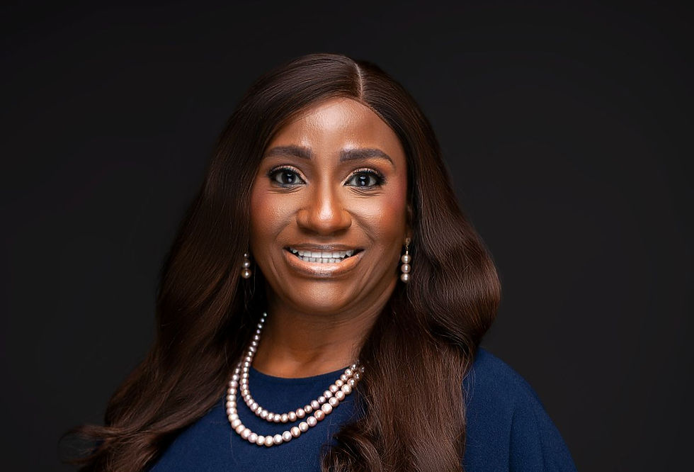 Smiling woman with long brown hair, wearing pearl earrings and necklace, and a navy top. Black background.