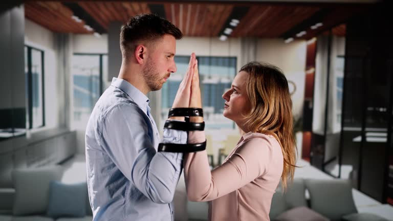 a man and a woman facing each other, pressing their palms together while their wrists are bound with black straps