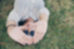 Person in sunglasses lying on grass, wearing a patterned shirt, hands raised towards the camera in a heart shape, relaxed mood.