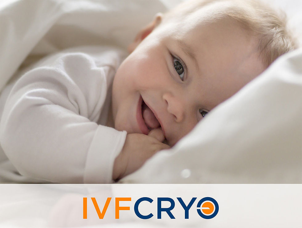 Smiling baby in white clothes lying on a bed, looking at the camera. Text "IVFCRYO" in orange and blue at the bottom.