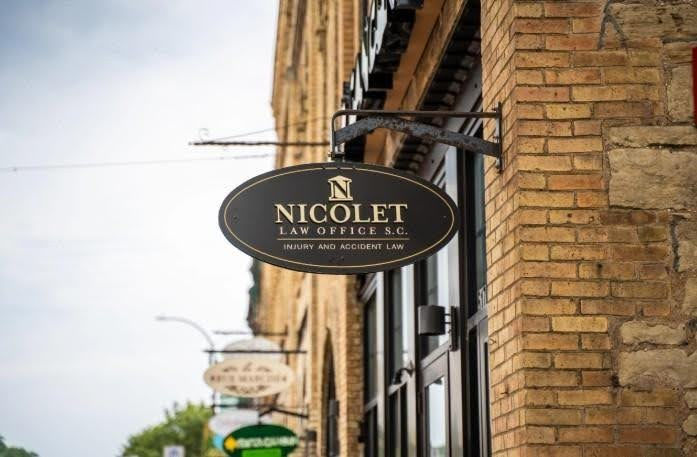 Hanging oval sign for Nicolet Law Office S.C. on a brick building, with Injury and Accident Law text in a quiet street scene