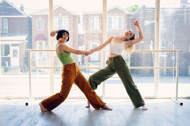 Two women are performing a contemporary dance pose together in a bright studio.