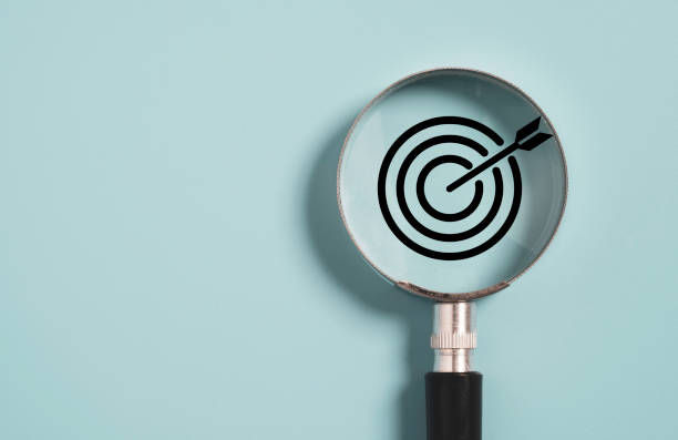 A magnifying glass focuses on a black target with an arrow on a light blue background, symbolizing precision and focus.