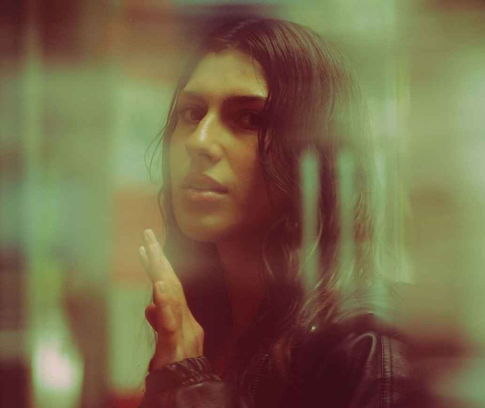 A woman gazes through a foggy window with a hand raised, creating a mysterious mood. The background is blurred with soft green hues.