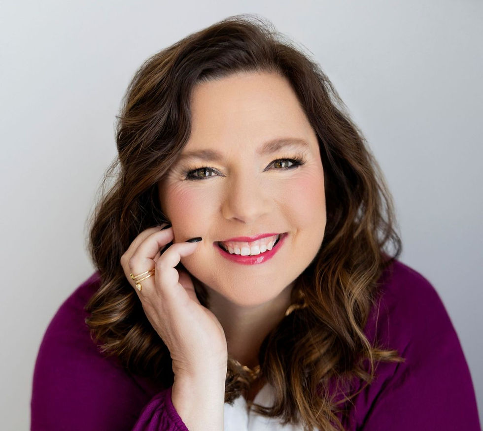 Smiling woman portrait with hand on cheek, wearing a purple top against a plain gray background.