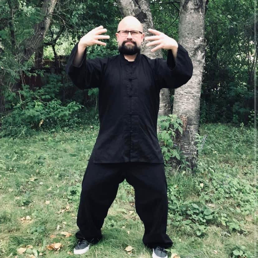 Man leads two horses over wooden poles in a grassy area with trees. Red boxes on ground. Overcast day creates a calm atmosphere.