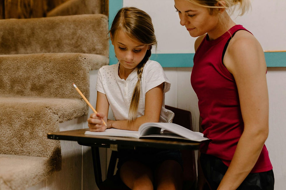 Girl with braid writing in a notebook, guided by woman in red tank top. They're near carpeted stairs, creating a focused learning scene.