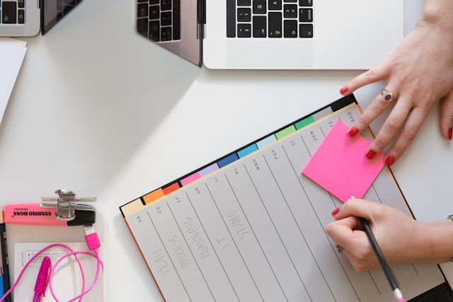 Person holding a pencil and a sticky note beside a table.