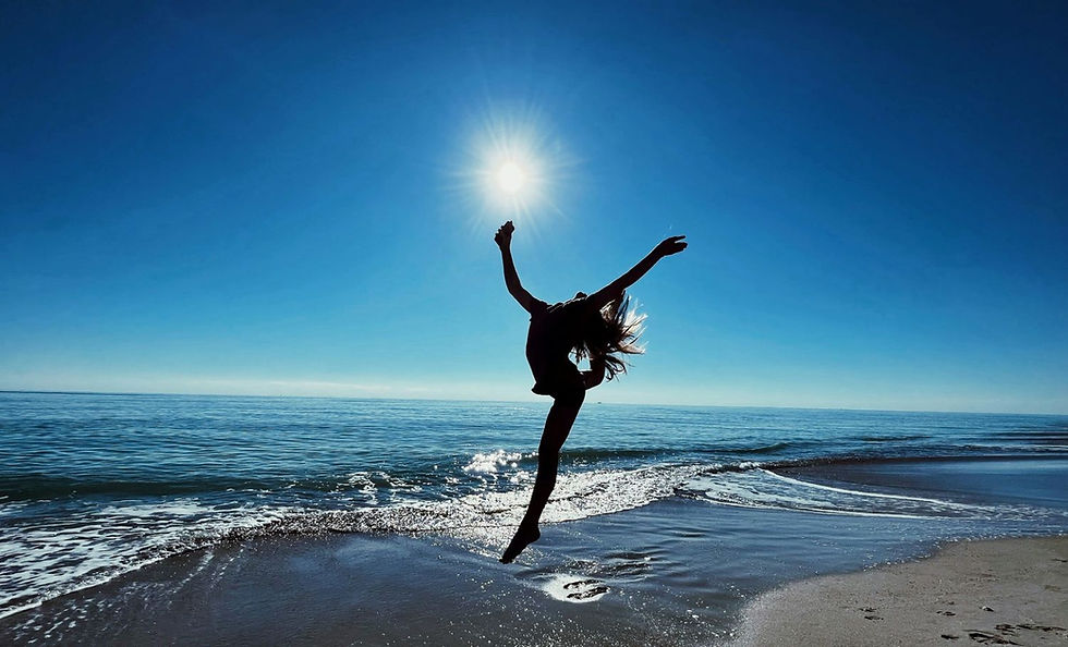 Silhouette of a person leaping joyfully on a beach with the sun shining brightly, blue sky, and calm ocean waves in the background.