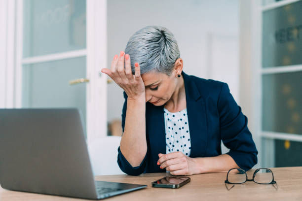 Frustrated businesswoman with head in hands sitting on desk in the office