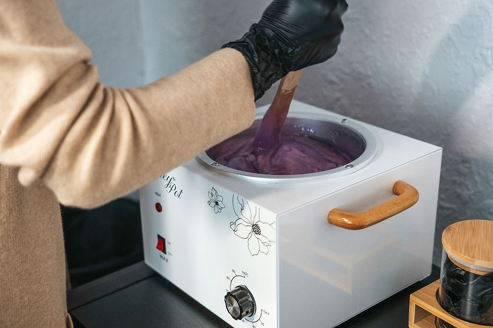 Person wearing a glove stirs purple wax in a white heater with floral design, against a textured wall background.