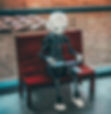A humanoid robot sits on a wooden bench, holding a tablet. It faces a large window overlooking a grassy area. The mood is calm.