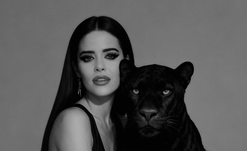 Woman in a black dress poses with a black panther against a gray background. Both have a calm, intense expression. Black-and-white image.