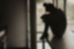 Silhouette of a person sitting on a kitchen counter, knees hugged to chest, near a window. The mood is contemplative and subdued.