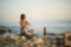 Woman meditating in yoga pose by stacked stones on a sandy beach. Warm sunset hues, peaceful ocean in the background.