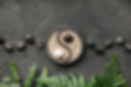 Yin-yang pebble arrangement on dark stone, framed by green fern leaves, with a calm zen mood