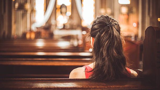 A woman inside a solemn church sitting on a bench facing the altar.