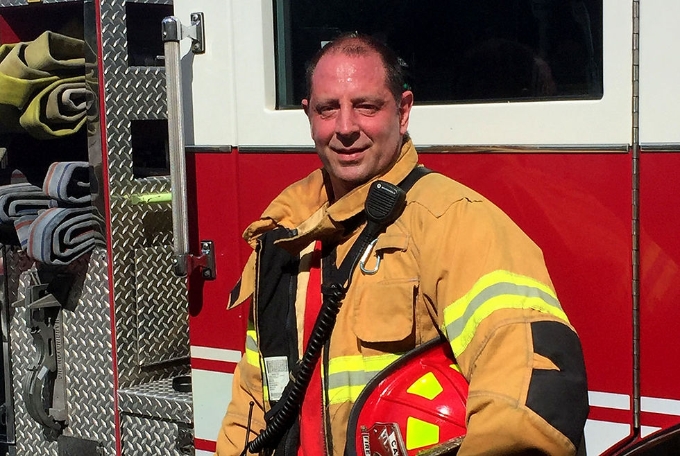 a man wearing a firefighter's full protective outfit under the heat of the sun, beside a firetruck