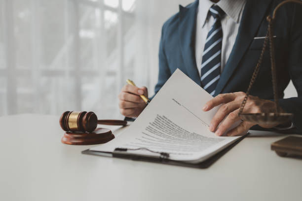 Lawyer in a suit reviews documents at a desk with a gavel, in a bright office, suggesting focused legal work.