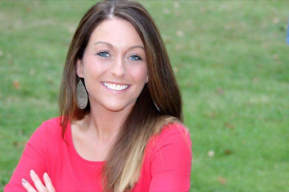 Smiling woman in a bright pink top with silver earrings, standing outdoors on a grassy background.