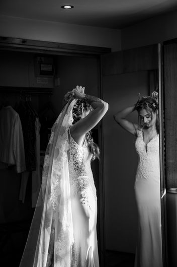 Black and white portrait of a bride placing the veil in her hair in front of a long mirror.