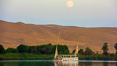 Dahabeya naviguant sur le Nil entre les palmeraies et les reliefs désertiques d’Égypte