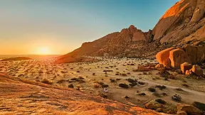 Roches de Spitzkoppe au coucher du soleil avec une piste et un véhicule dans les paysages arides de Namibie