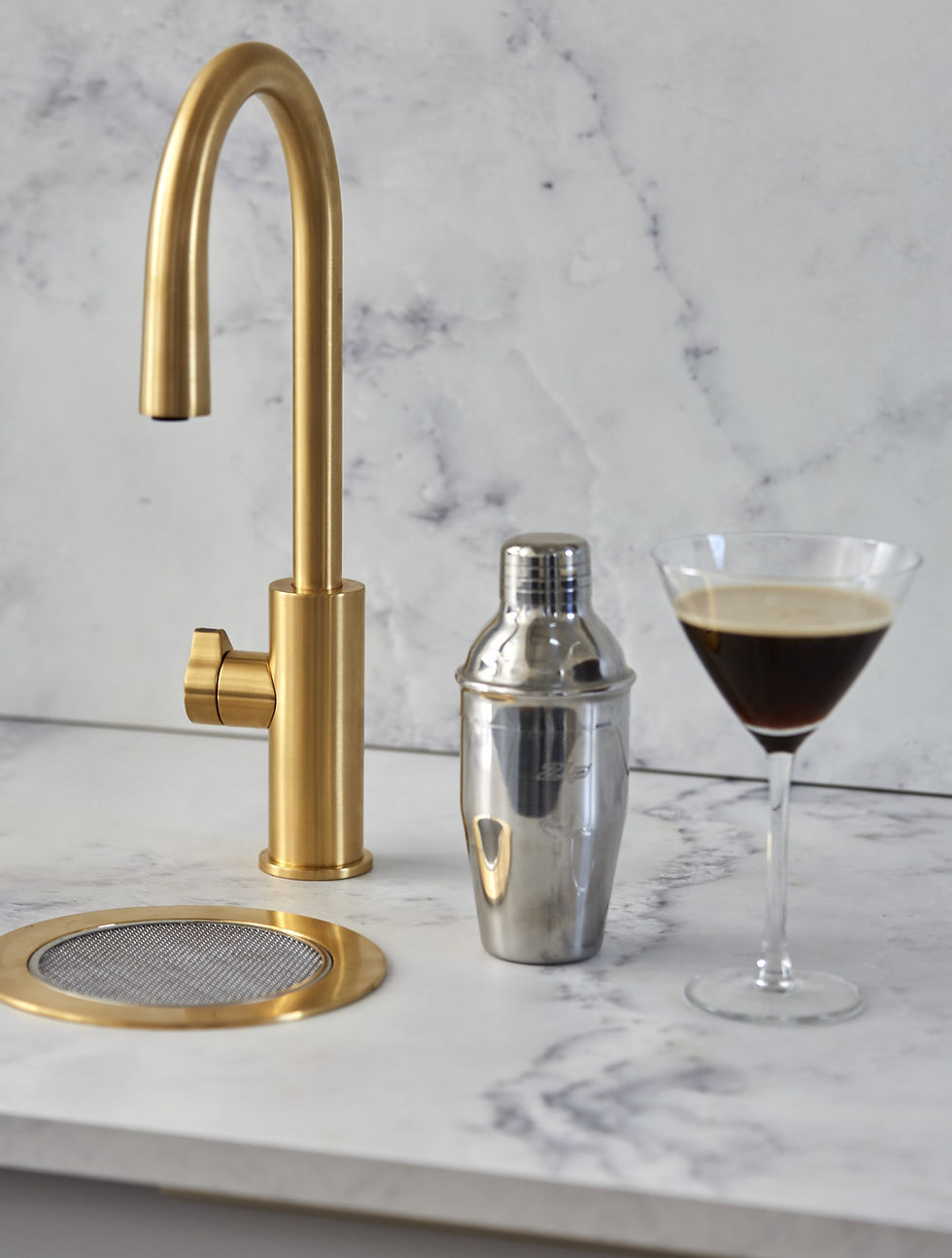 Gold HydroTap and matching gold font on a marble counter, with a silver cocktail shaker and a martini glass with brown liquid.