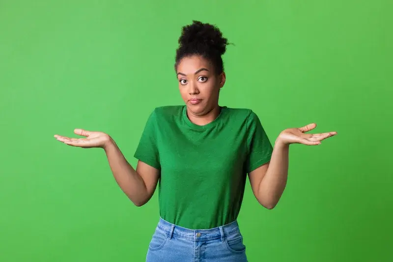 Woman in green shirt and jeans shrugging with an uncertain expression against a solid green background.