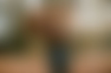 Child in blue jacket holds large bundle of autumn leaves, standing in sunlit forest with fallen foliage on the ground, creating a cozy mood.