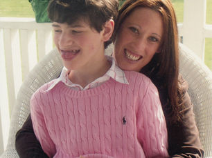 Cari and her son Logan, who has Angelman syndrome, smiling together on a porch.