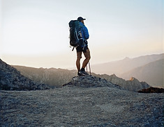 man in black jacket and blue denim shorts with black hiking backpack standing on mountain