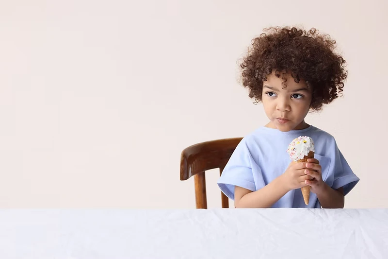 Un petit garçon métisse assis à table prêt à manger une glace.
