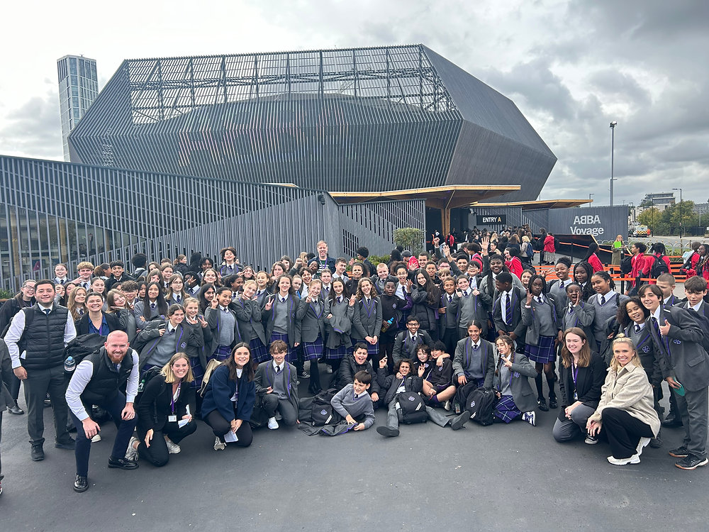 Large group posing for a photo outside a modern stadium or arena with a patterned facade.